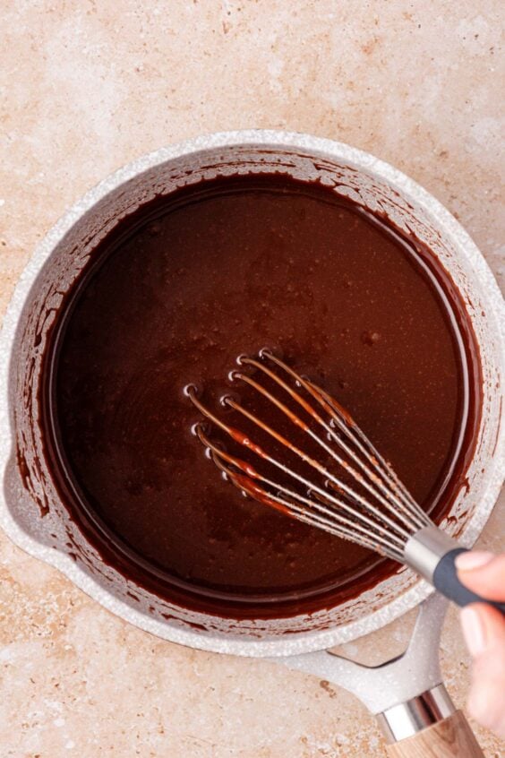 Chocolate icing being whisked in a pot.