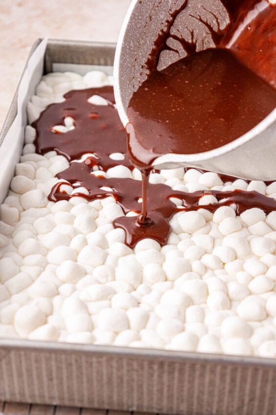 Hot chocolate icing being poured over marshmallows in a cake pan.