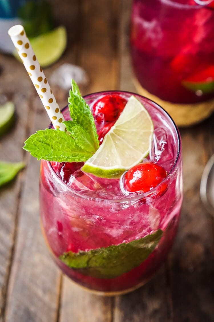 A glass filled with cranberry mojito punch on a wooden table.