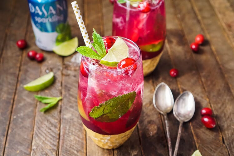 A glass filled with a cranberry mojito on a wooden table.