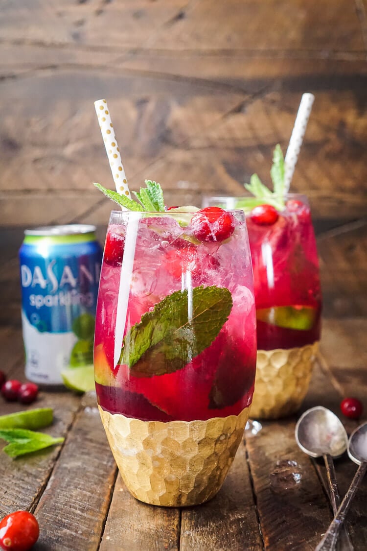 Two glasses filled with cranberry mojito punch on a wooden table.