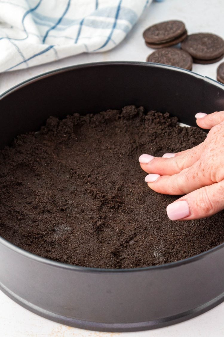 A woman's hand pressing oreo crumbs into a springform pan.