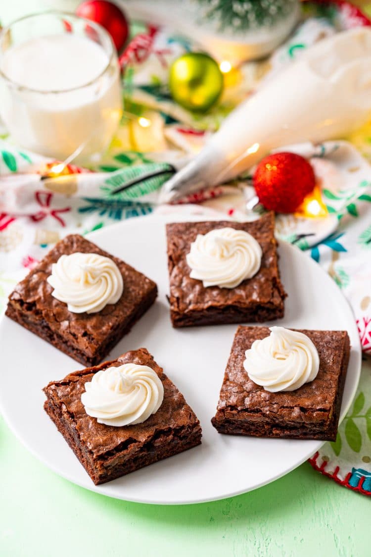 Brownies on a white plate with swirls of buttercream frosting on them and holiday decorations scattered around.