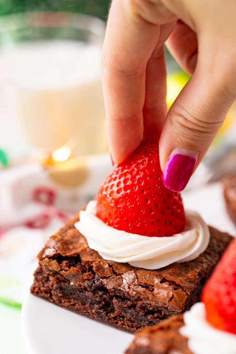 A woman's hand placing a strawberry on top of a frosted brownie.