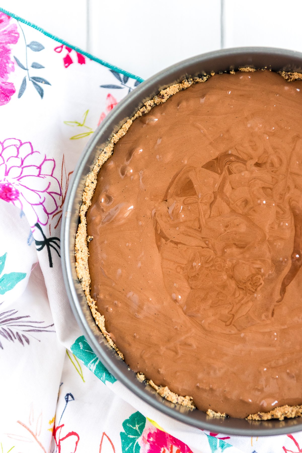 Brownie batter poured into a graham cracker pie crust in a spring form pan.
