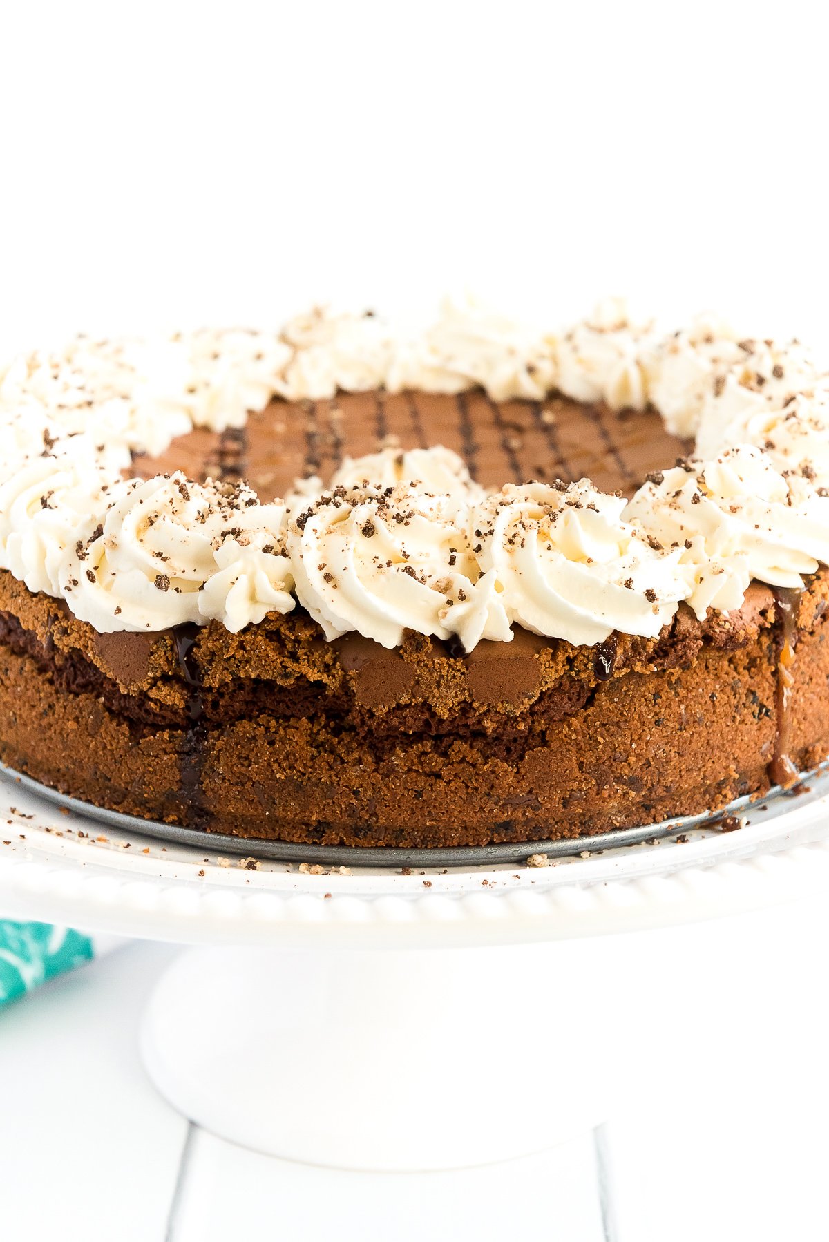 Brownie pie on a cake stand topped with chocolate and caramel drizzle and whipped cream.