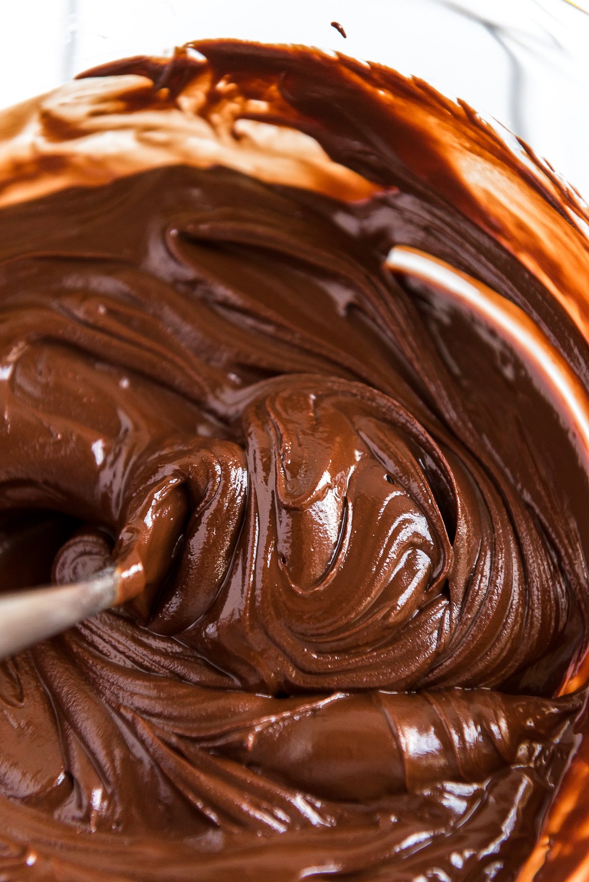 Melted chocolate chips and butter being stirred in a glass bowl.