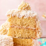 A slice of yellow coconut cake being lifted away from the whole cake.