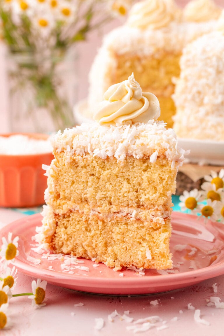 A slice of coconut cake on a pink plate on a table.