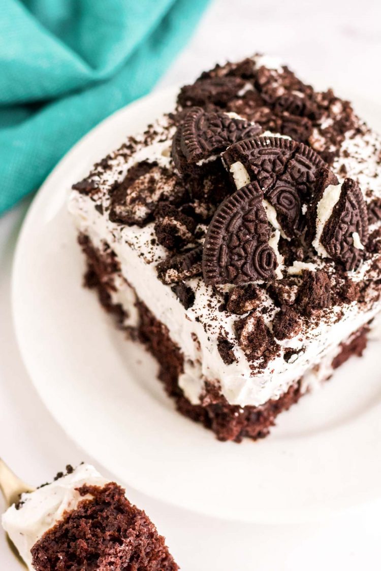 Slightly angled photo of a piece of Oreo chocolate cake on a white plate with a teal napkin next to it.