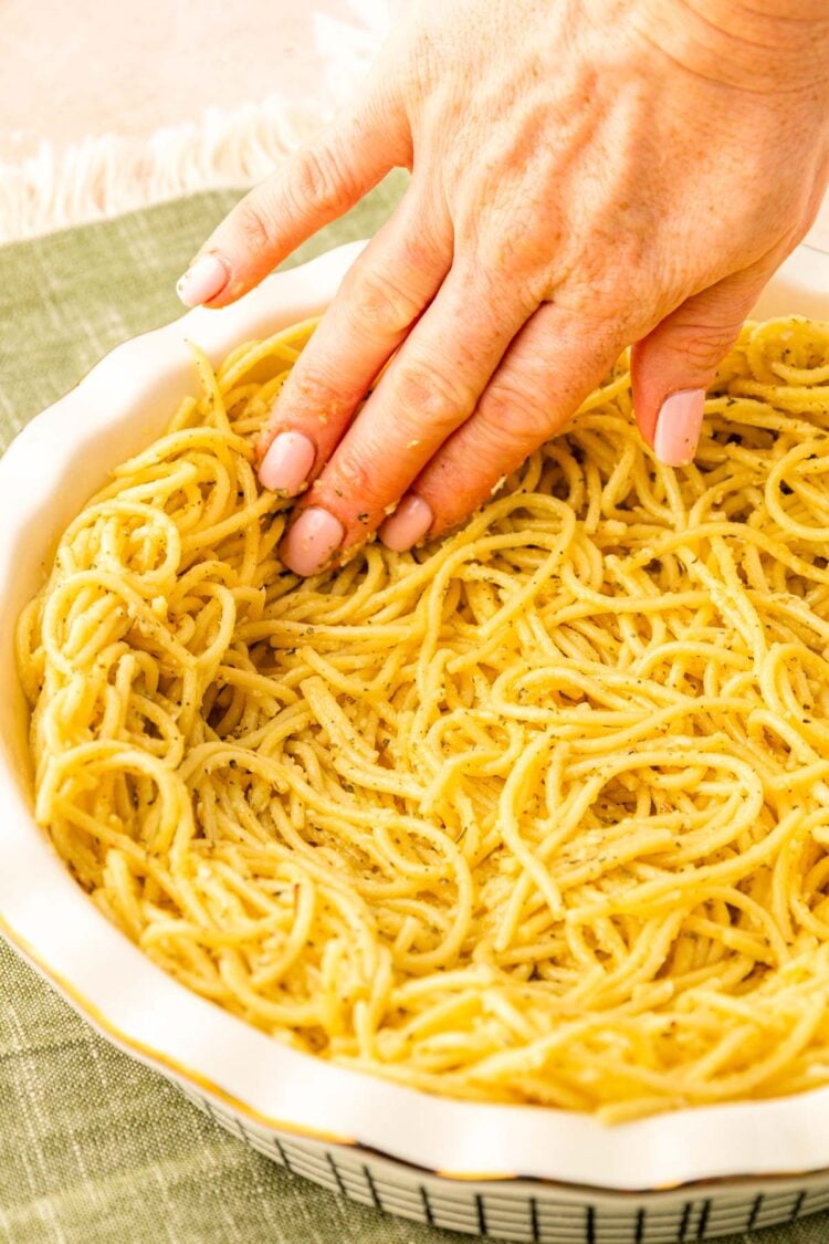 Spaghetti being pressed into a pie dish.