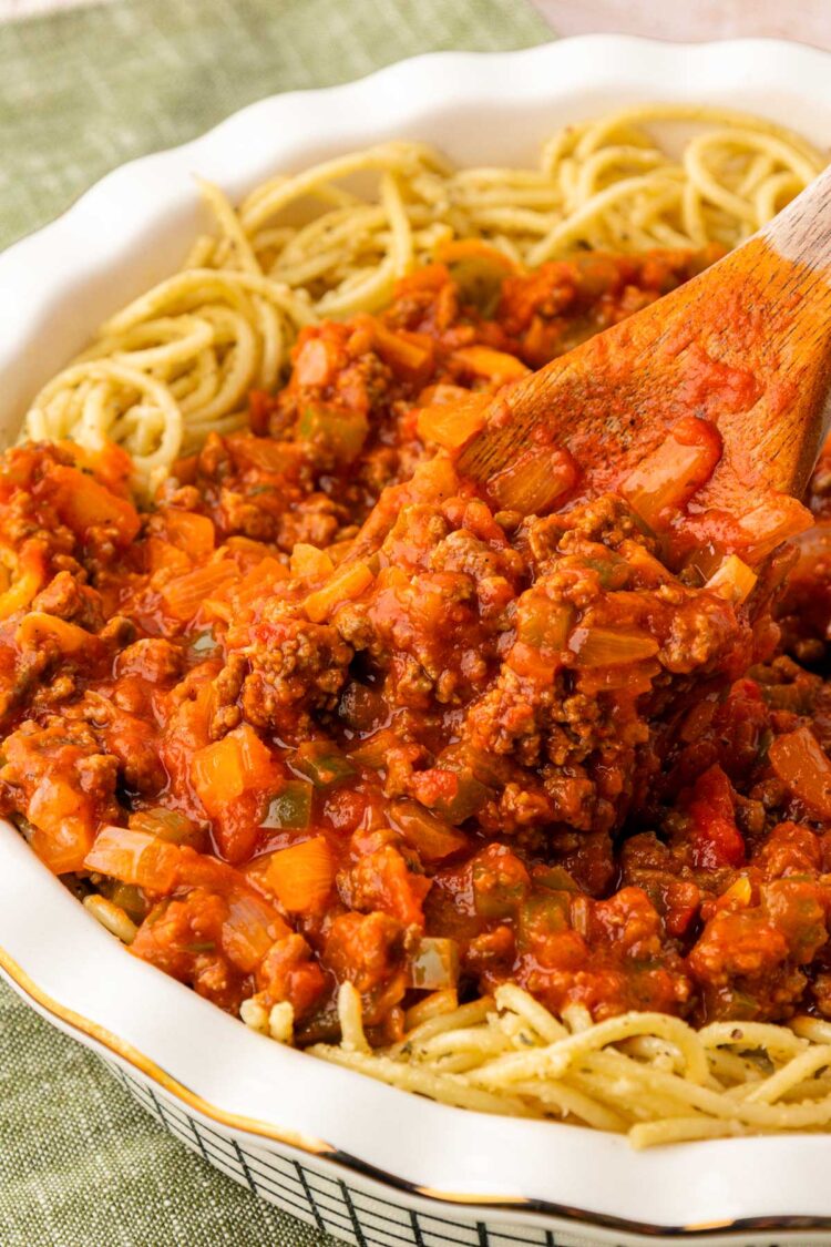 Bolognese Sauce being added to the center of a pie dish filled with spaghetti.