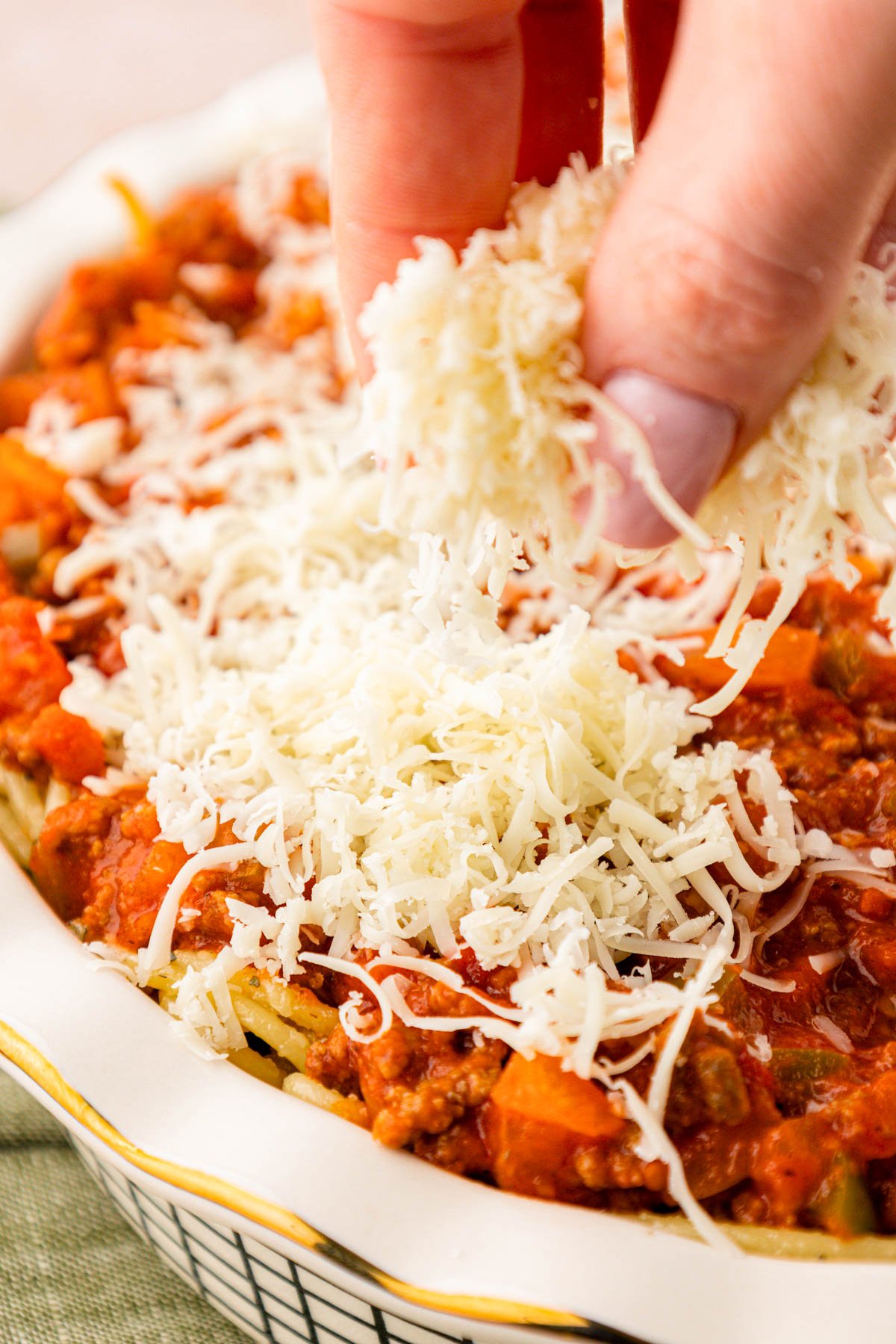 Shredded mozzarella being added to a spaghetti pie.