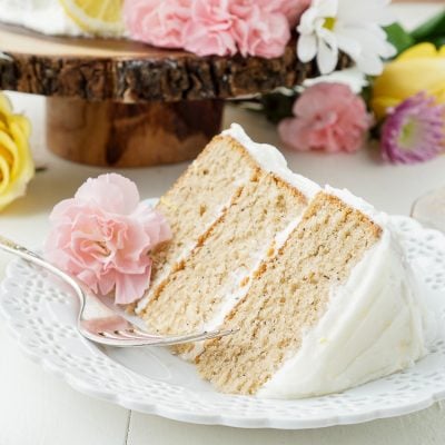 A slice of earl grey layer cake on a white plate with flowers around it.