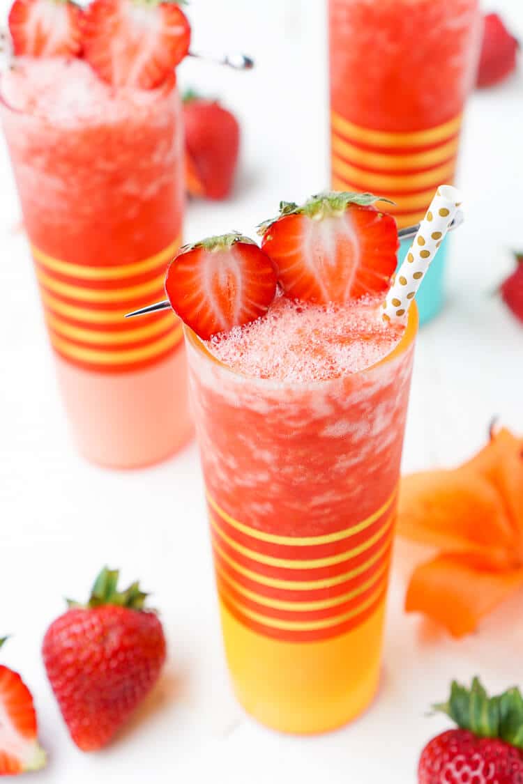 Close up photo of a frozen strawberry daiquiri in a gold striped glass with other drinks in the background.