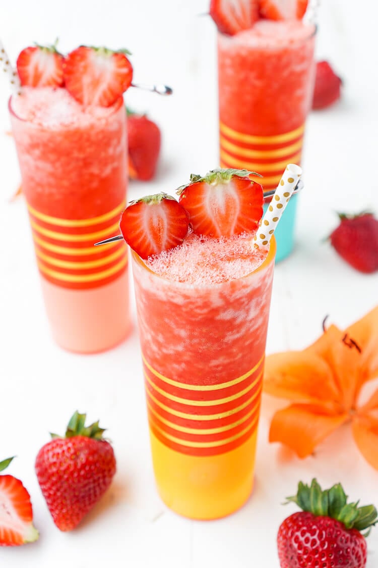 Three Frozen Strawberry Daiquiris on a white table with fresh strawberries scattered around.