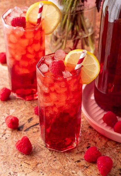 Two glasses of raspberry iced tea on a table.