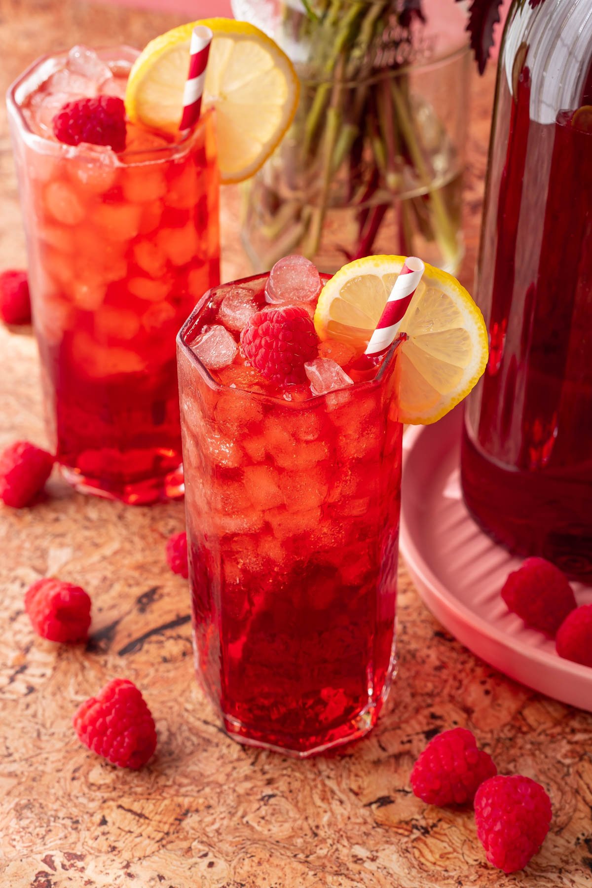 Two glasses of raspberry iced tea on a table.