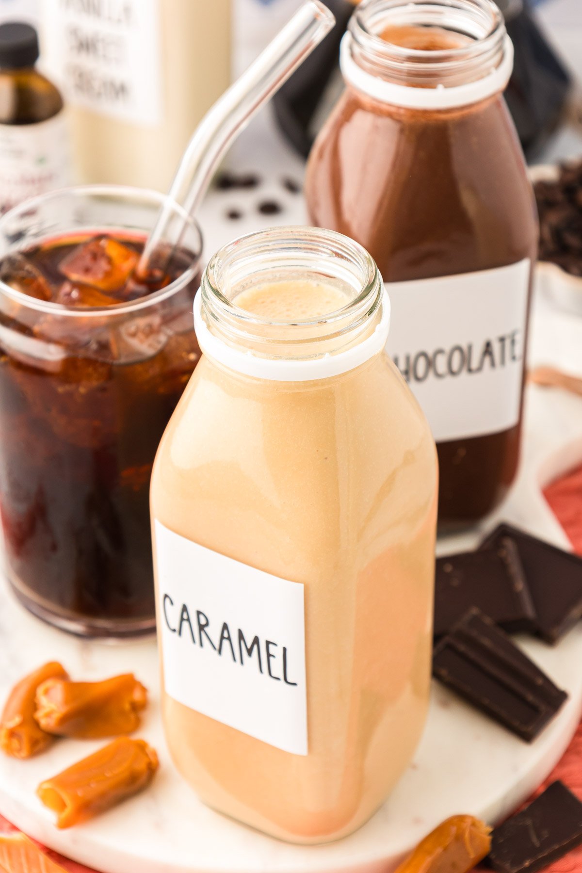 Bottles of homemade coffee creamer next to a glass of iced coffee.