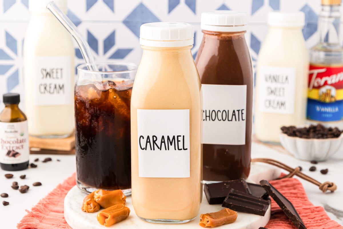 Bottles of homemade coffee creamer next to a glass of iced coffee.