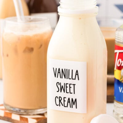 A bottle of vanilla sweet creamer coffee creamer on a table with iced coffee in the background.