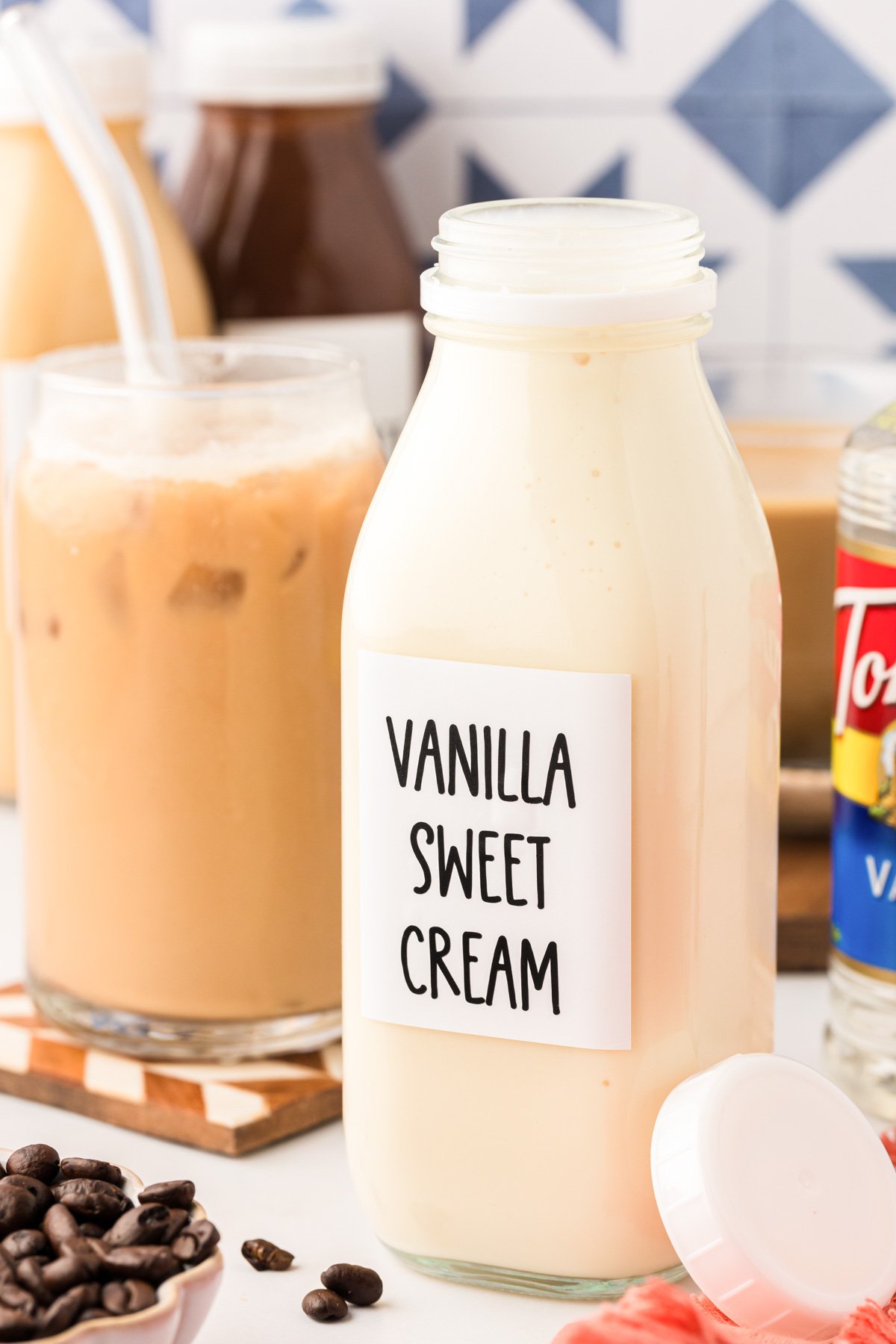 A bottle of vanilla sweet creamer coffee creamer on a table with iced coffee in the background.