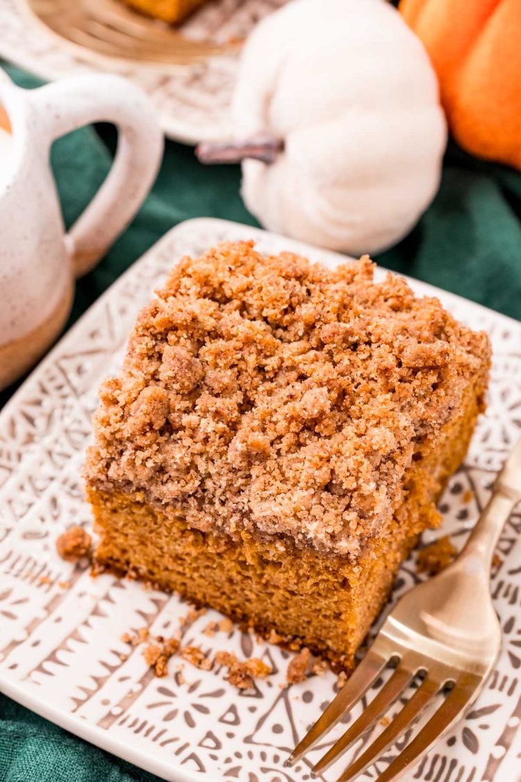 Close up photo of a slice of pumpkin coffee cake on a tan plate on a green napkin with a gold fork resting next to it.