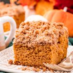 Close up photo of a slice of pumpkin coffee cake on a plate on a green napkin with fall decor in the background.