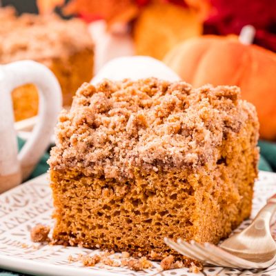 Close up photo of a slice of pumpkin coffee cake on a plate on a green napkin with fall decor in the background.