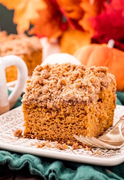 Close up photo of a slice of pumpkin coffee cake on a plate on a green napkin with fall decor in the background.