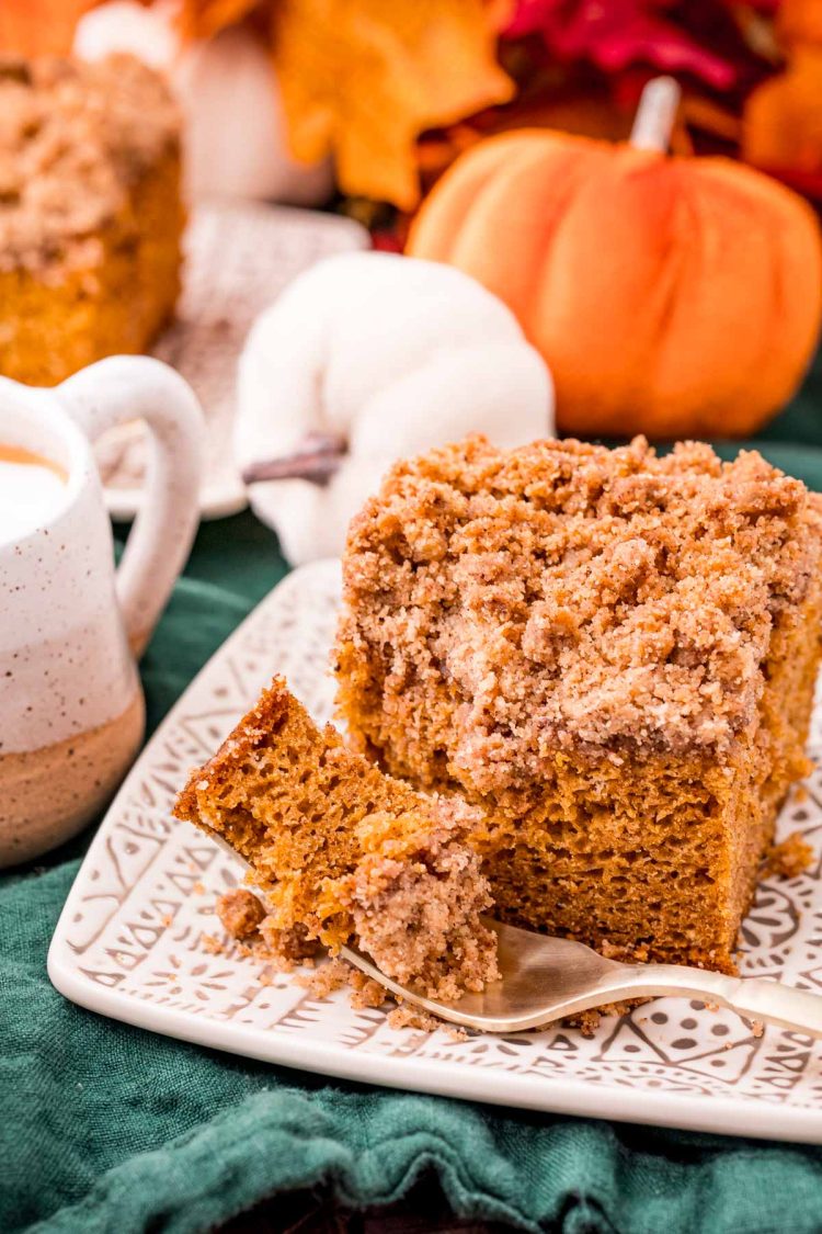 Pumpkin coffee cake on a patterned plate on a green napkin with a fork resting on the plate with a bite of cake on it.