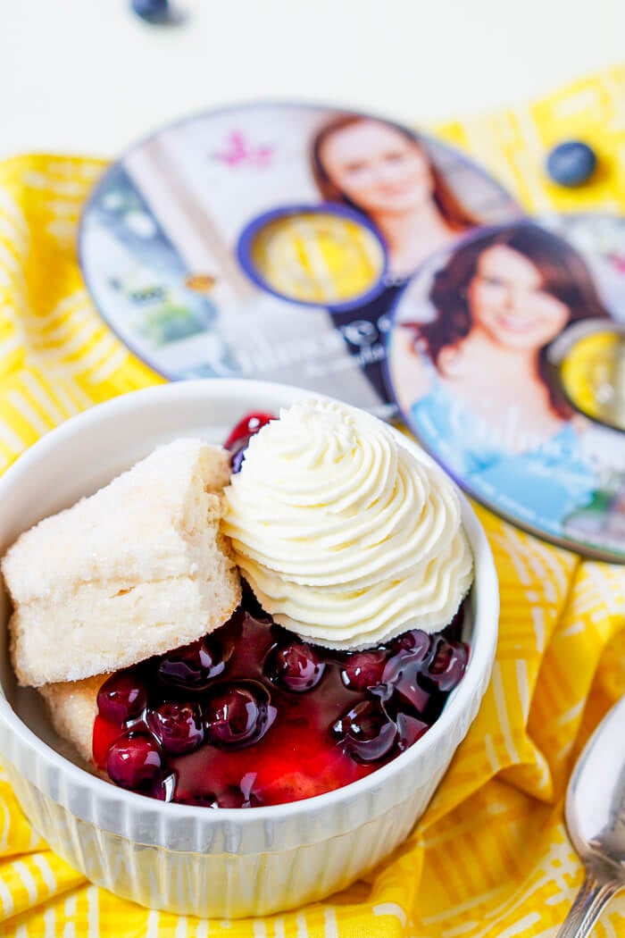 A bowl with cake, cherries and whipped cream in in next to two CDs of the Gilmore Girls 