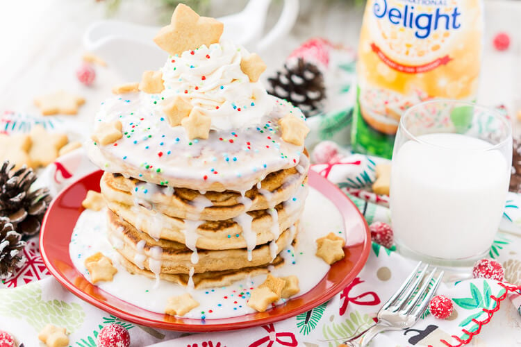 These Sugar Cookie Pancakes will add holiday cheer to your morning routine. Trade in traditional buttermilk for thick, fluffy, and sweet ricotta based pancakes laced with sugar cookie creamer, and topped with baked sugar cookies, icing, whipped cream, and sprinkles!