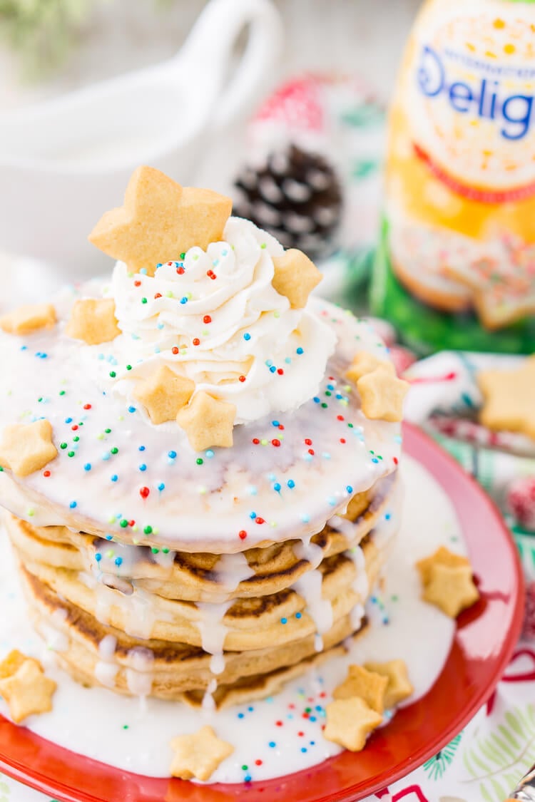 These Sugar Cookie Pancakes will add holiday cheer to your morning routine. Trade in traditional buttermilk for thick, fluffy, and sweet ricotta based pancakes laced with sugar cookie creamer, and topped with baked sugar cookies, icing, whipped cream, and sprinkles!