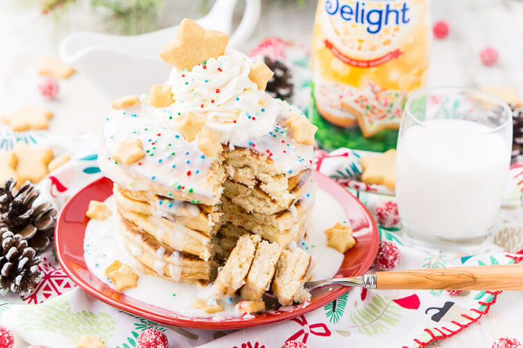 These Sugar Cookie Pancakes will add holiday cheer to your morning routine. Trade in traditional buttermilk for thick, fluffy, and sweet ricotta based pancakes laced with sugar cookie creamer, and topped with baked sugar cookies, icing, whipped cream, and sprinkles!
