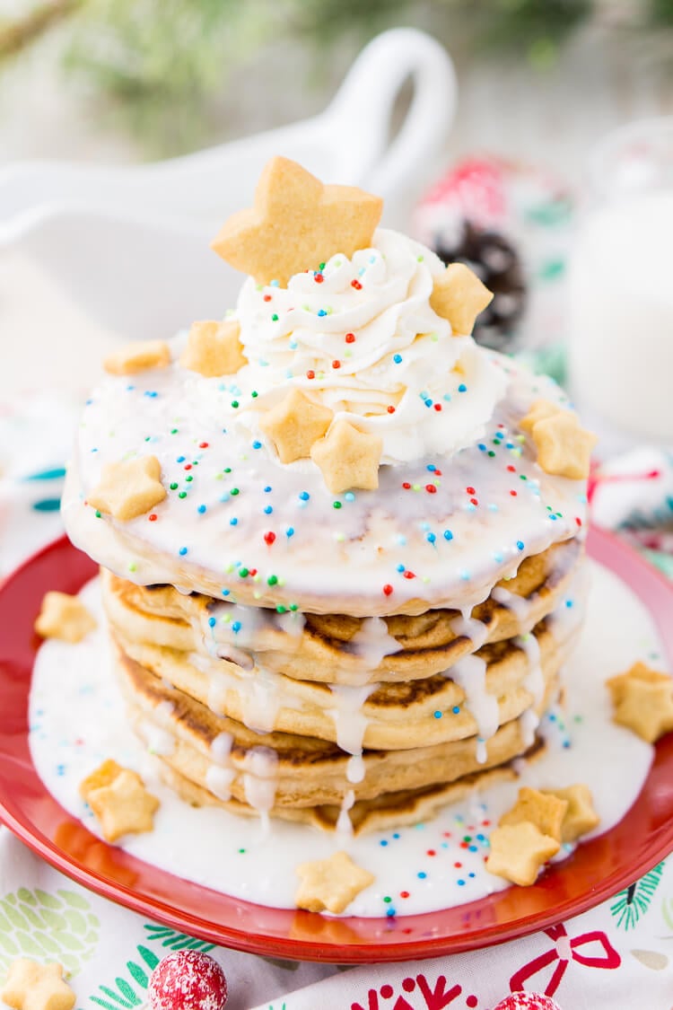 These Sugar Cookie Pancakes will add holiday cheer to your morning routine. Trade in traditional buttermilk for thick, fluffy, and sweet ricotta based pancakes laced with sugar cookie creamer, and topped with baked sugar cookies, icing, whipped cream, and sprinkles!