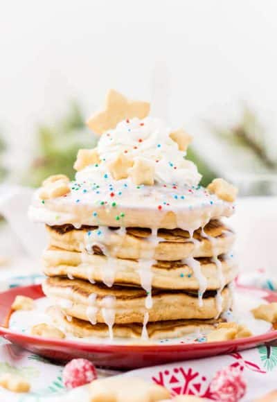 These Sugar Cookie Pancakes will add holiday cheer to your morning routine. Trade in traditional buttermilk for thick, fluffy, and sweet ricotta based pancakes laced with sugar cookie creamer, and topped with baked sugar cookies, icing, whipped cream, and sprinkles!