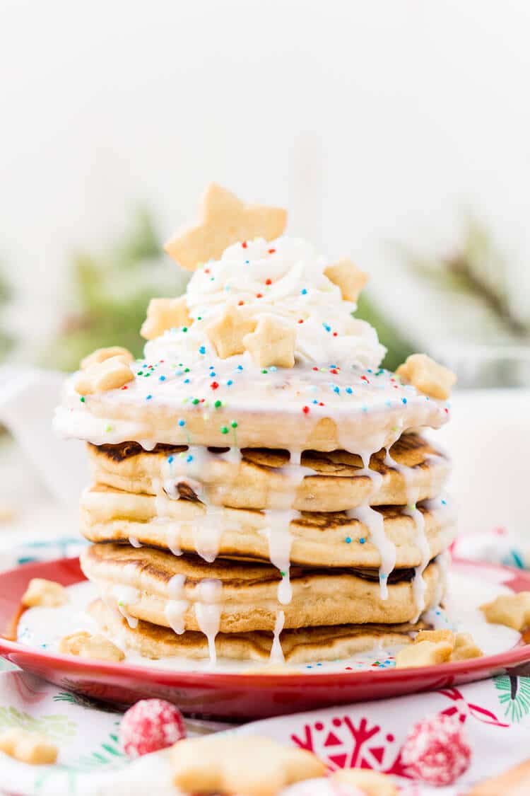 These Sugar Cookie Pancakes will add holiday cheer to your morning routine. Trade in traditional buttermilk for thick, fluffy, and sweet ricotta based pancakes laced with sugar cookie creamer, and topped with baked sugar cookies, icing, whipped cream, and sprinkles!