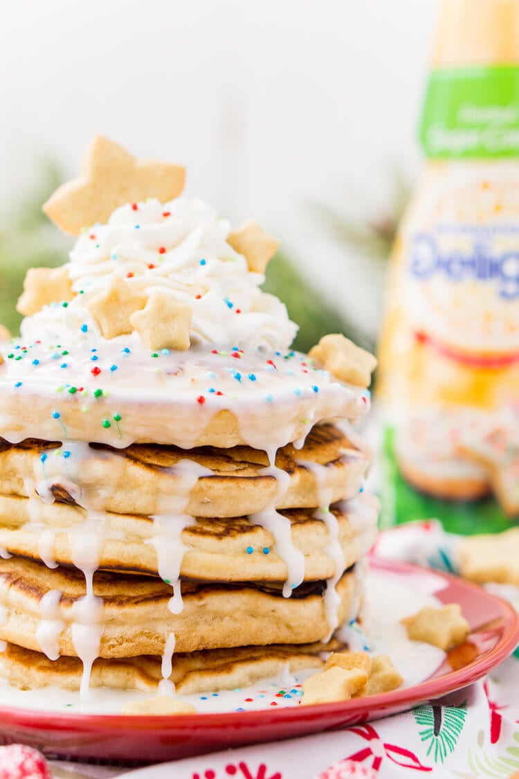 These Sugar Cookie Pancakes will add holiday cheer to your morning routine. Trade in traditional buttermilk for thick, fluffy, and sweet ricotta based pancakes laced with sugar cookie creamer, and topped with baked sugar cookies, icing, whipped cream, and sprinkles!