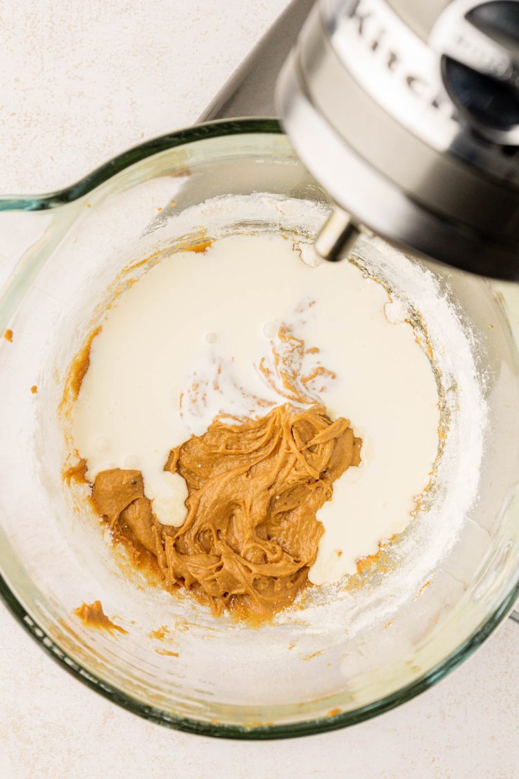 Heavy cream being added to a glass mixing bowl with batter.