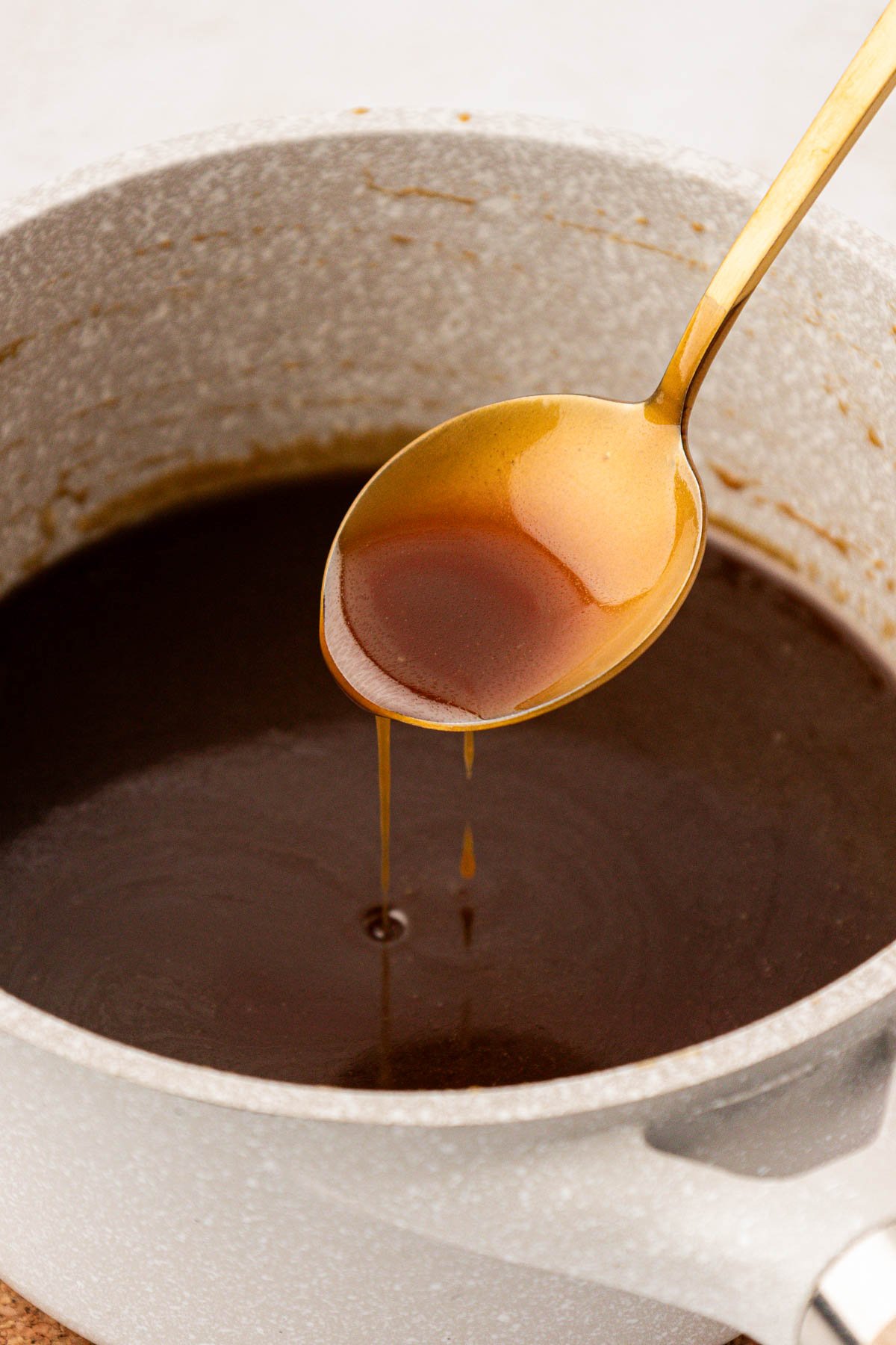 A gold spoon spooning toffee sauce out of a pot.