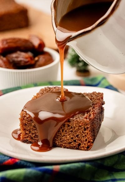 Toffee sauce being poured over the top of a slice of sticky toffee pudding.