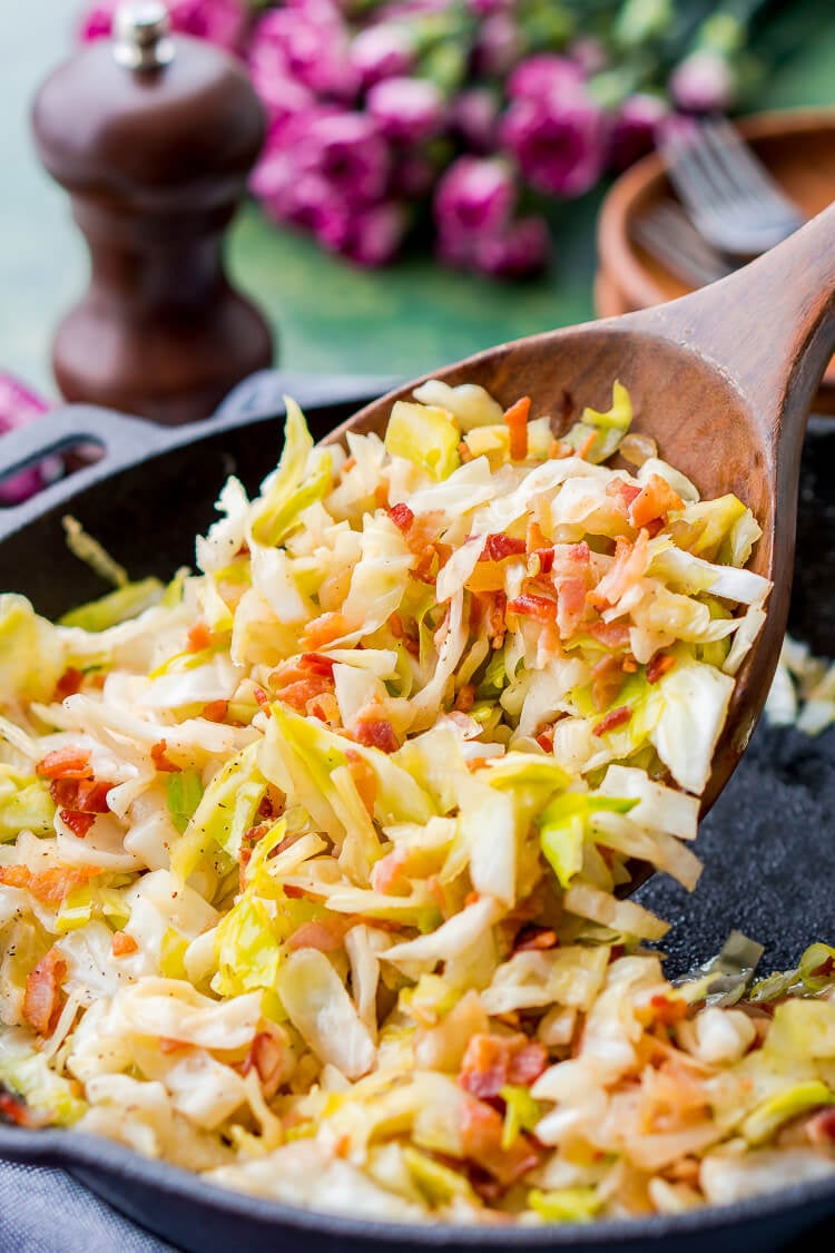 A wooden spoon scooping fried cabbage out of a skillet.