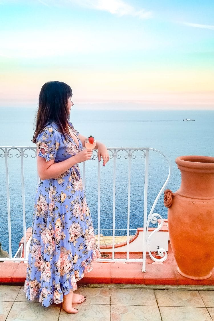 Woman Leaning on railing with drink looking at sunset