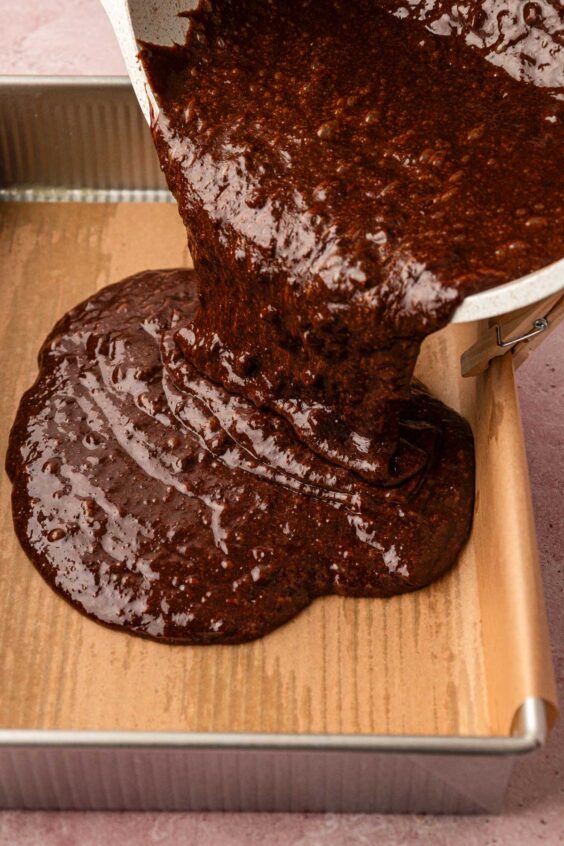 Brownie batter being poured into a prepared baking pan.