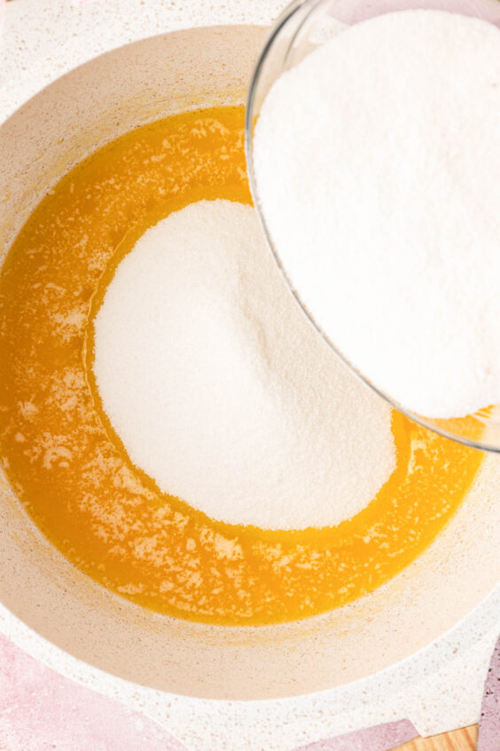 Sugar being added to melted butter in a pan.