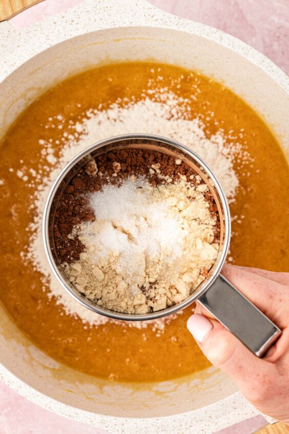 Dry ingredients being sifted into wet ingredients for brownies.