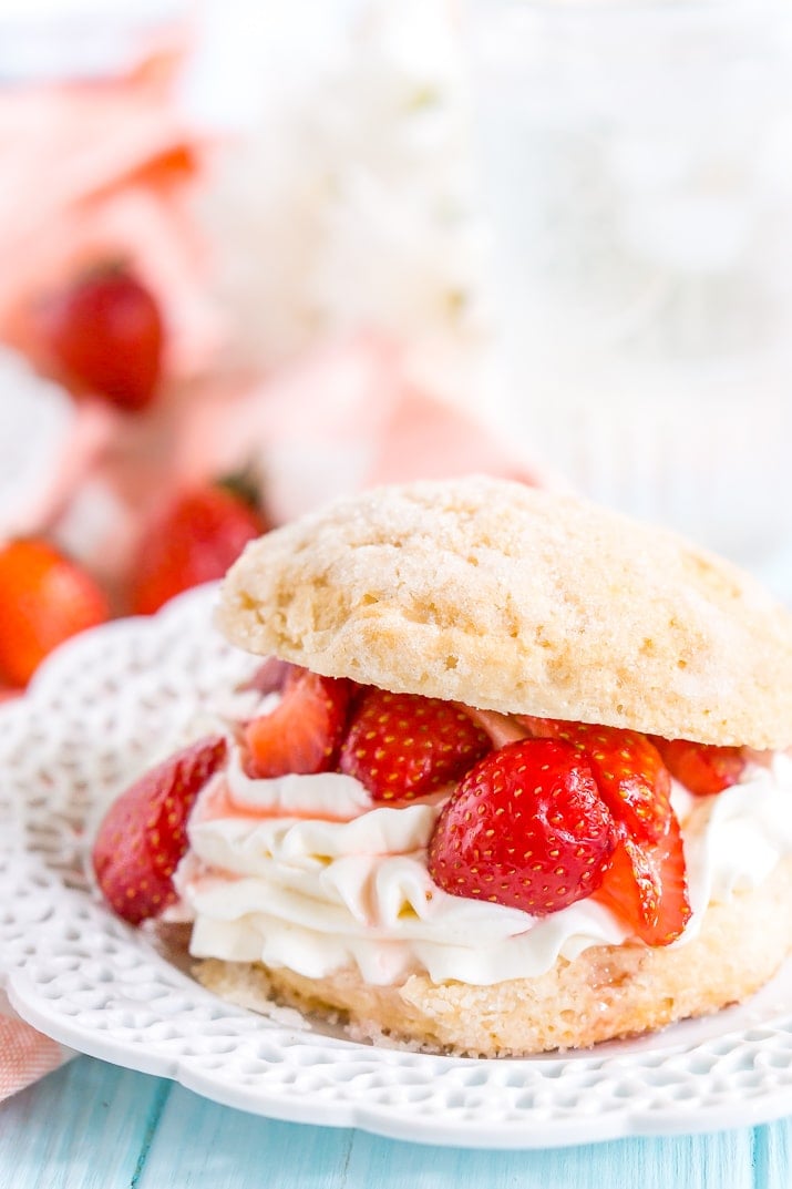 Close up photo of a prepared strawberry shortcake dessert on a white plat with more strawberries in the background.