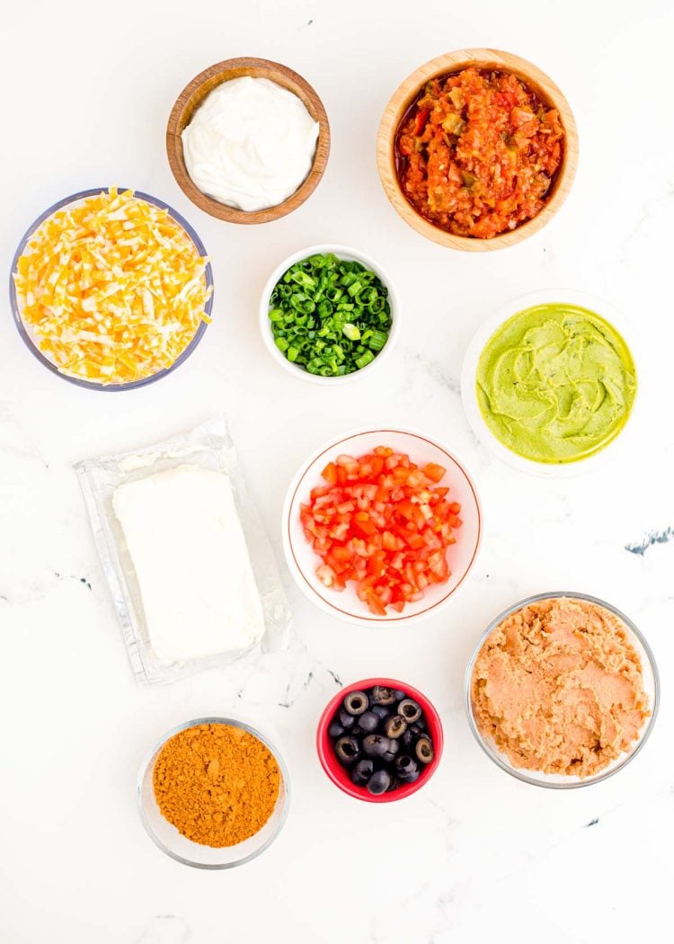 Ingredients to make 7 Layer Dip on a white marble surface.