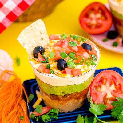 7 Layer Dip Cups on a small blue board on a yellow surface.